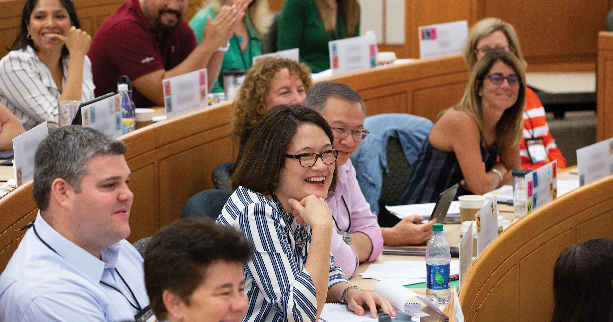 A diverse group of executives engaged in a discussion in an HBS exed classroom smiling and interacting