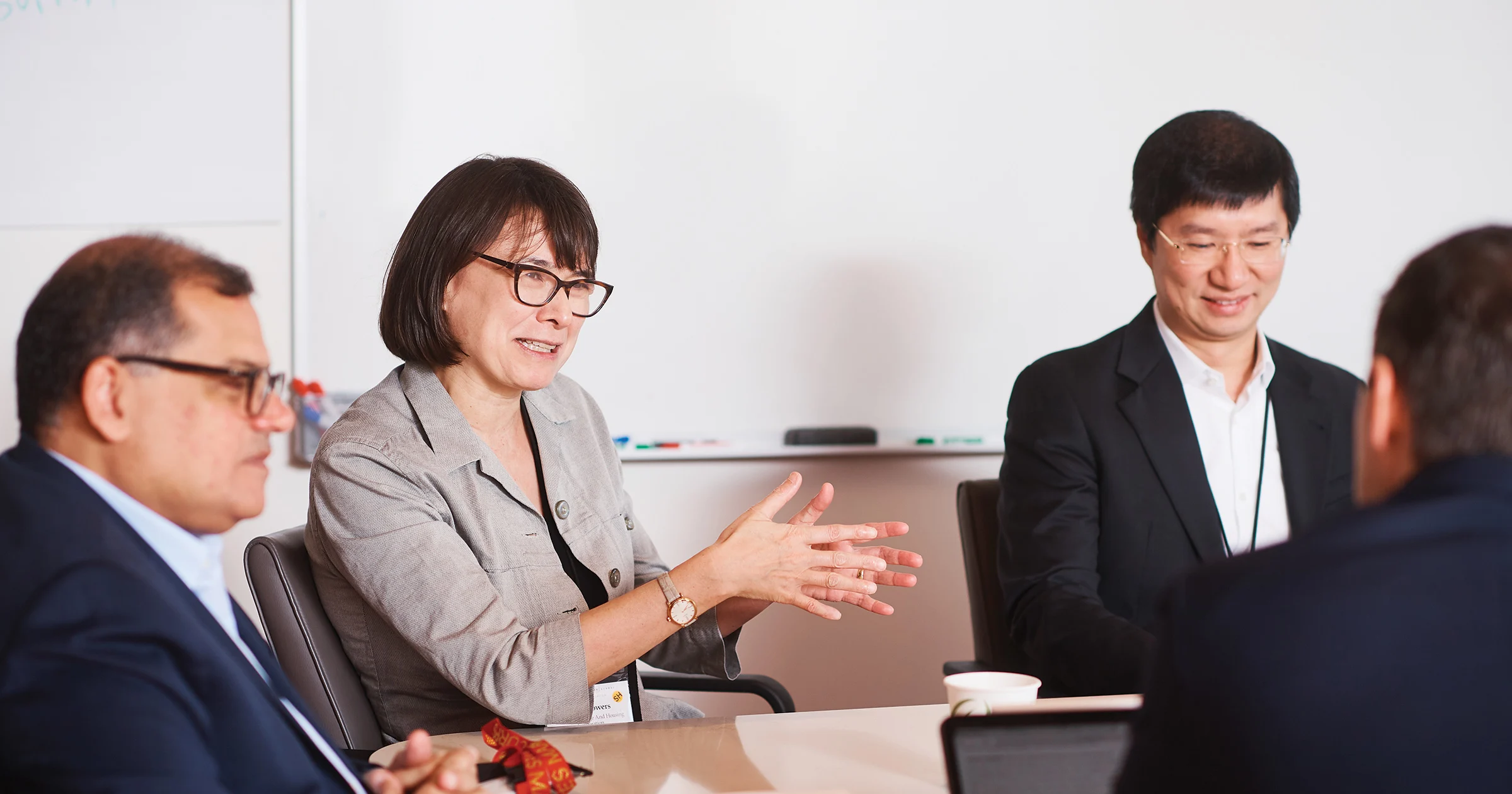 One professionally dressed female and three male executives wearing suits, engaged in conversation around a table during a study session 