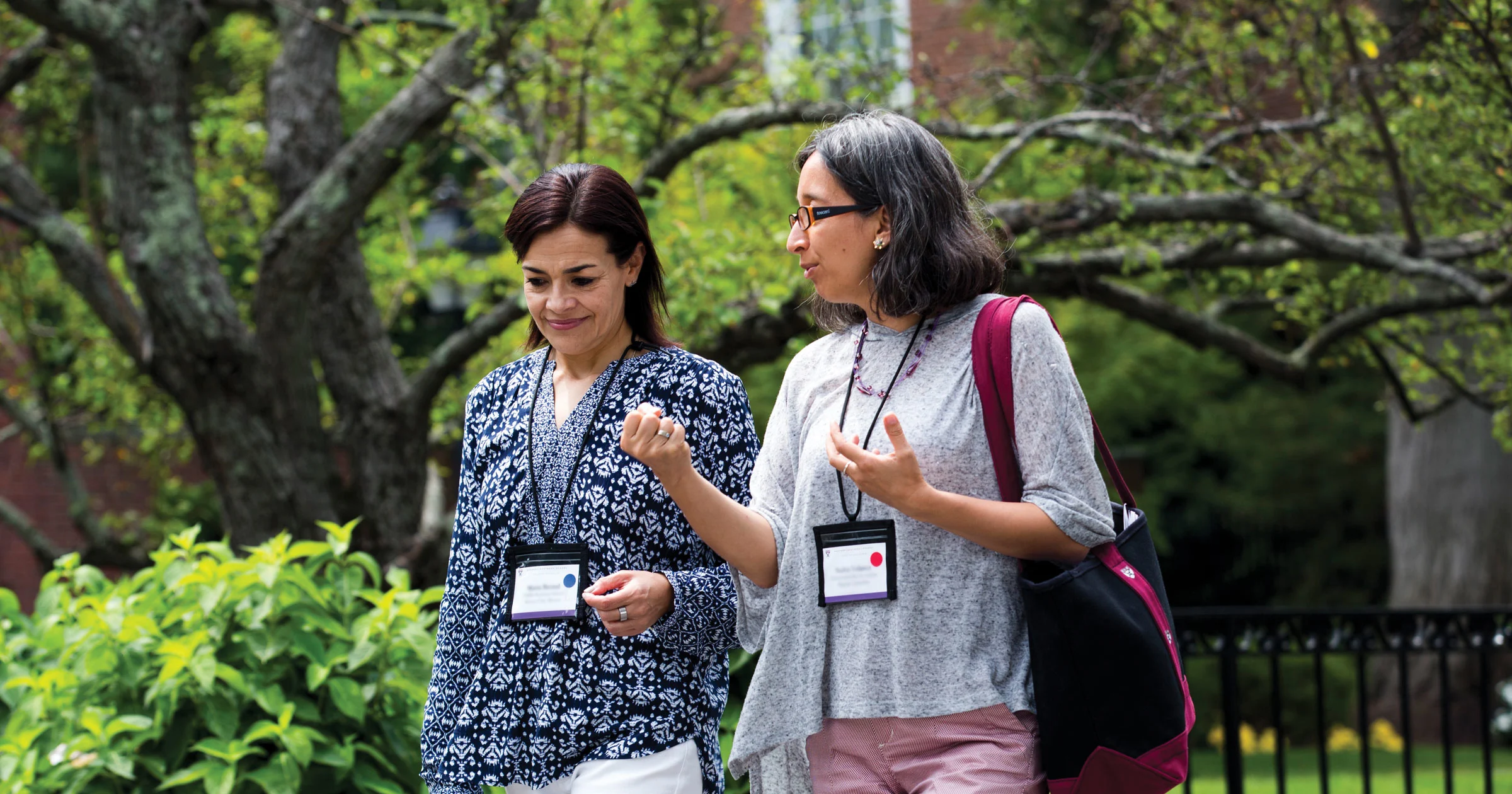 Two female executives wearing badges talk while walking on the HBS campus