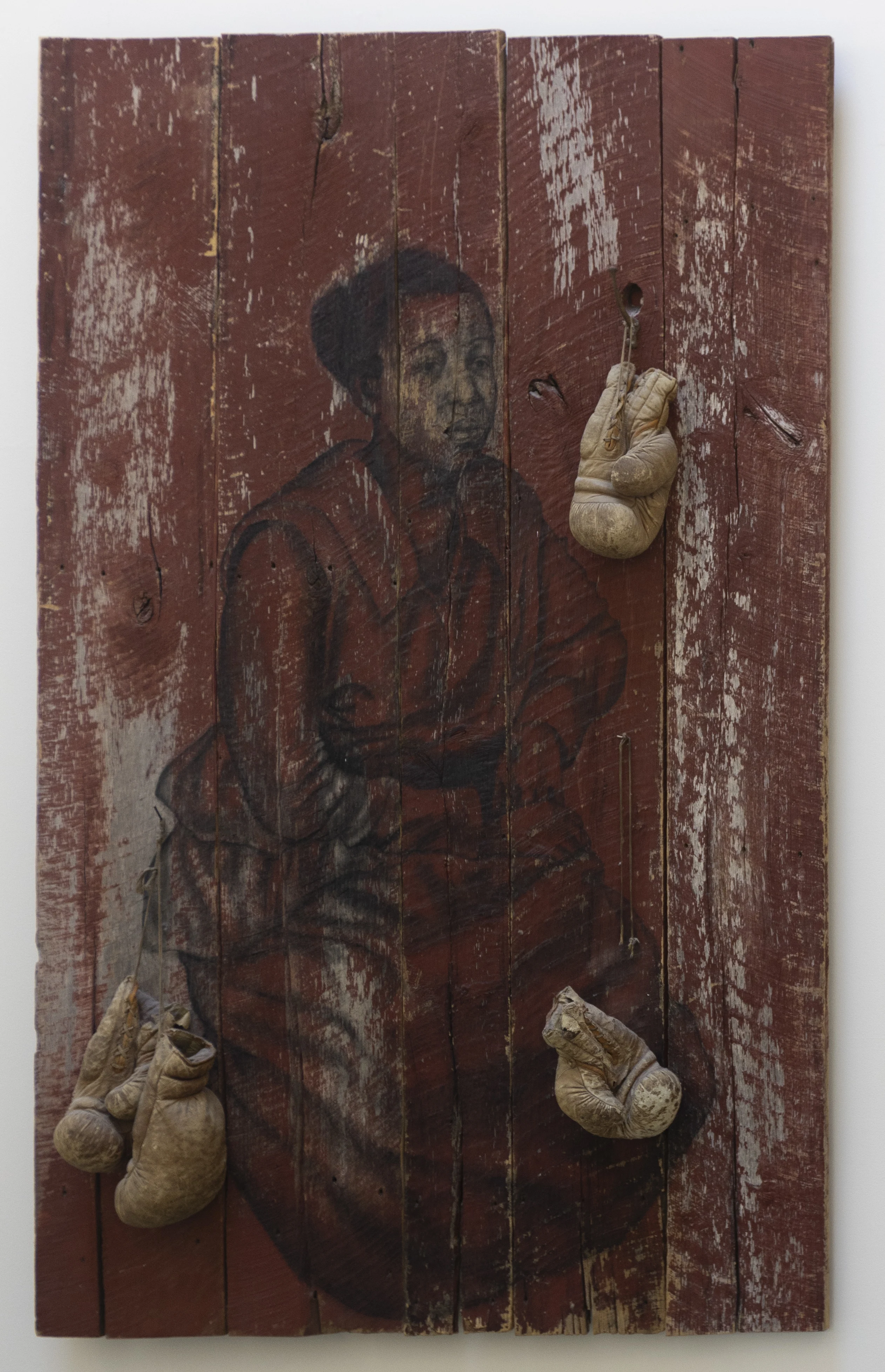 Charcoal portrait of a seated woman on distressed red wood, with four worn boxing gloves hanging on nails.