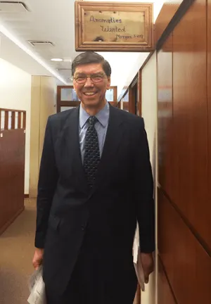 Clay Christensen poses with the Anomalies Wanted sign hanging outside his office