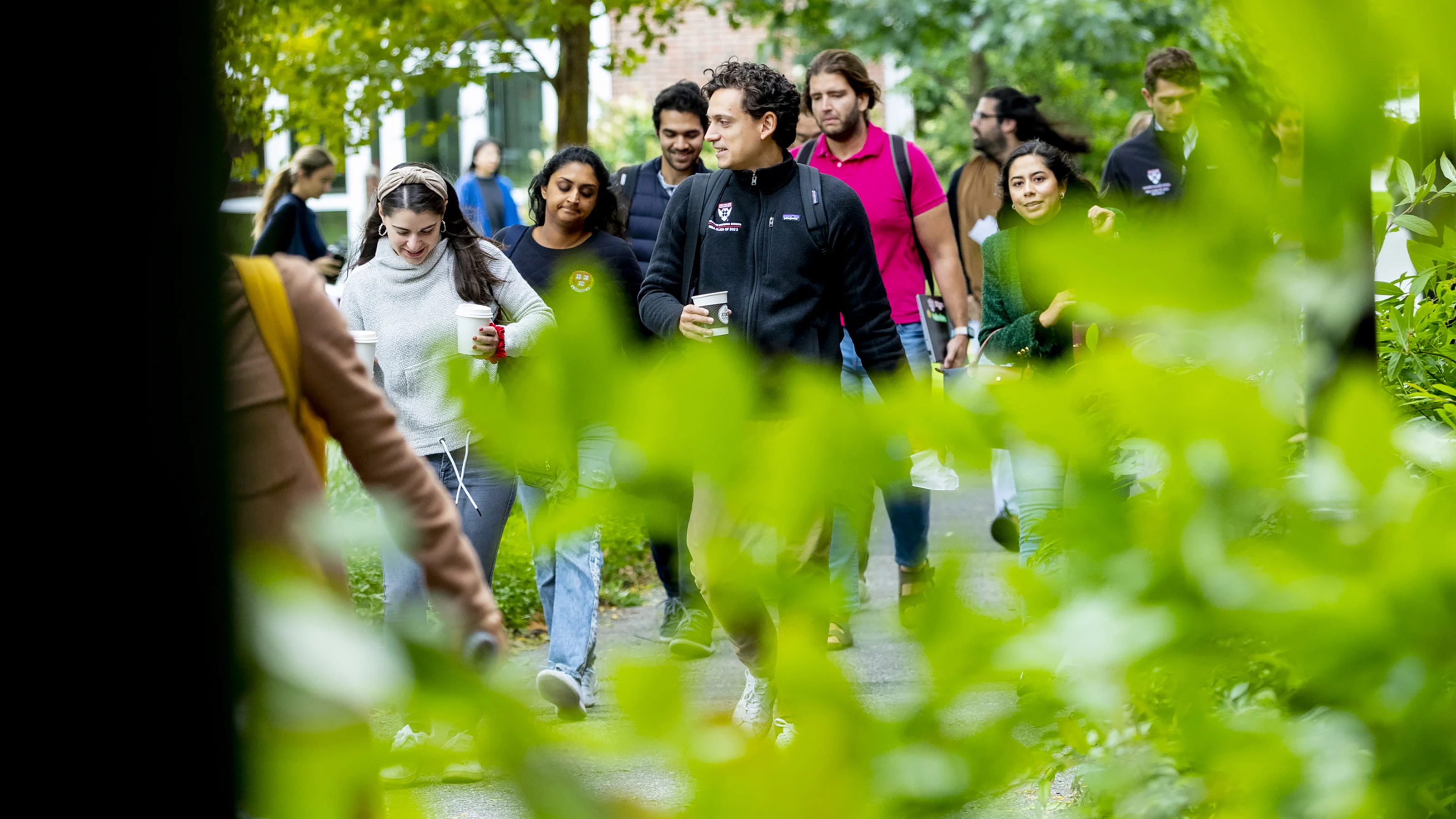 People sitting and walking on a grassy campus quad under blooming trees in front of a red-brick building.