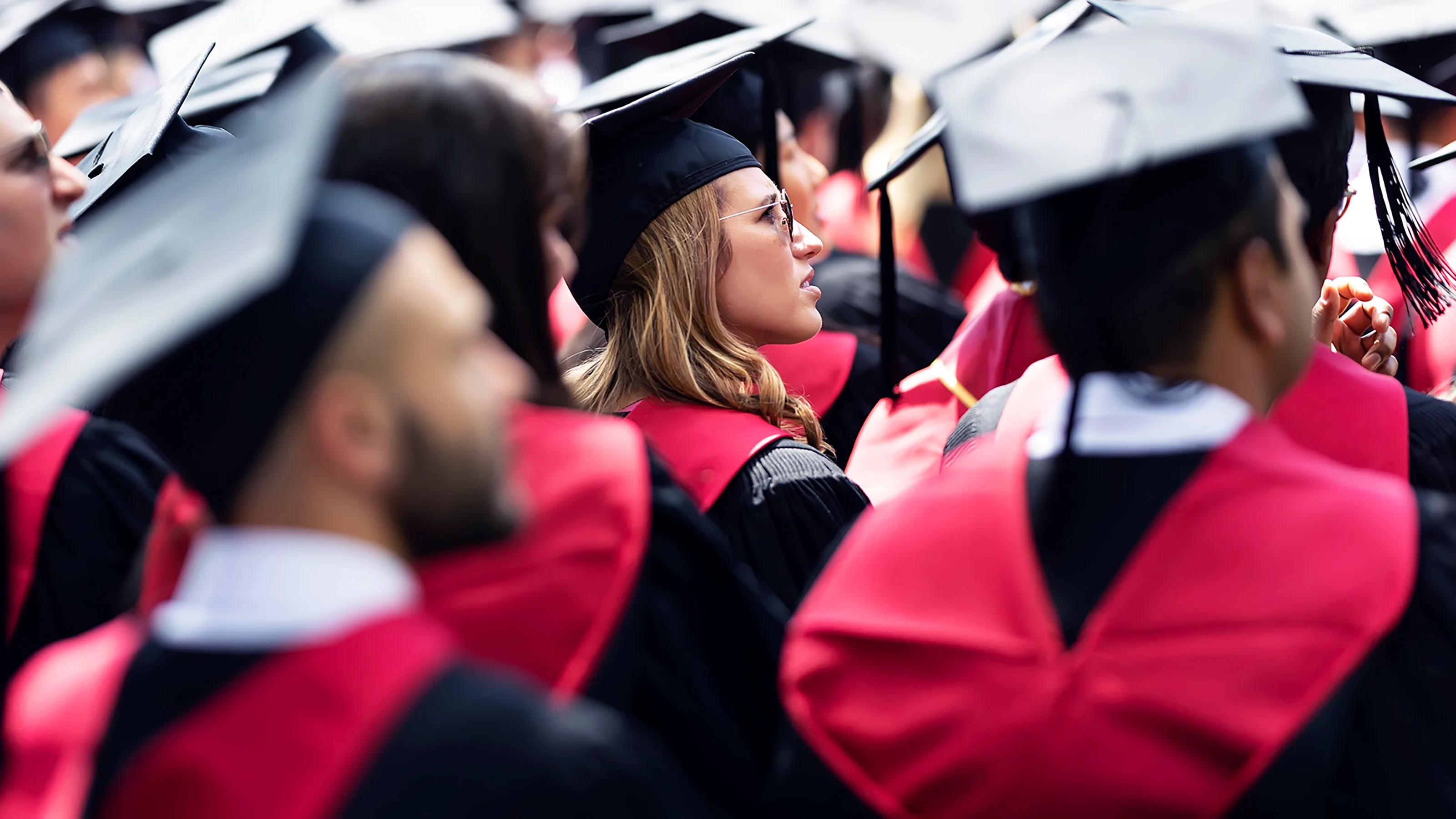 Outdoor commencement ceremony with graduates in robes facing a stage.