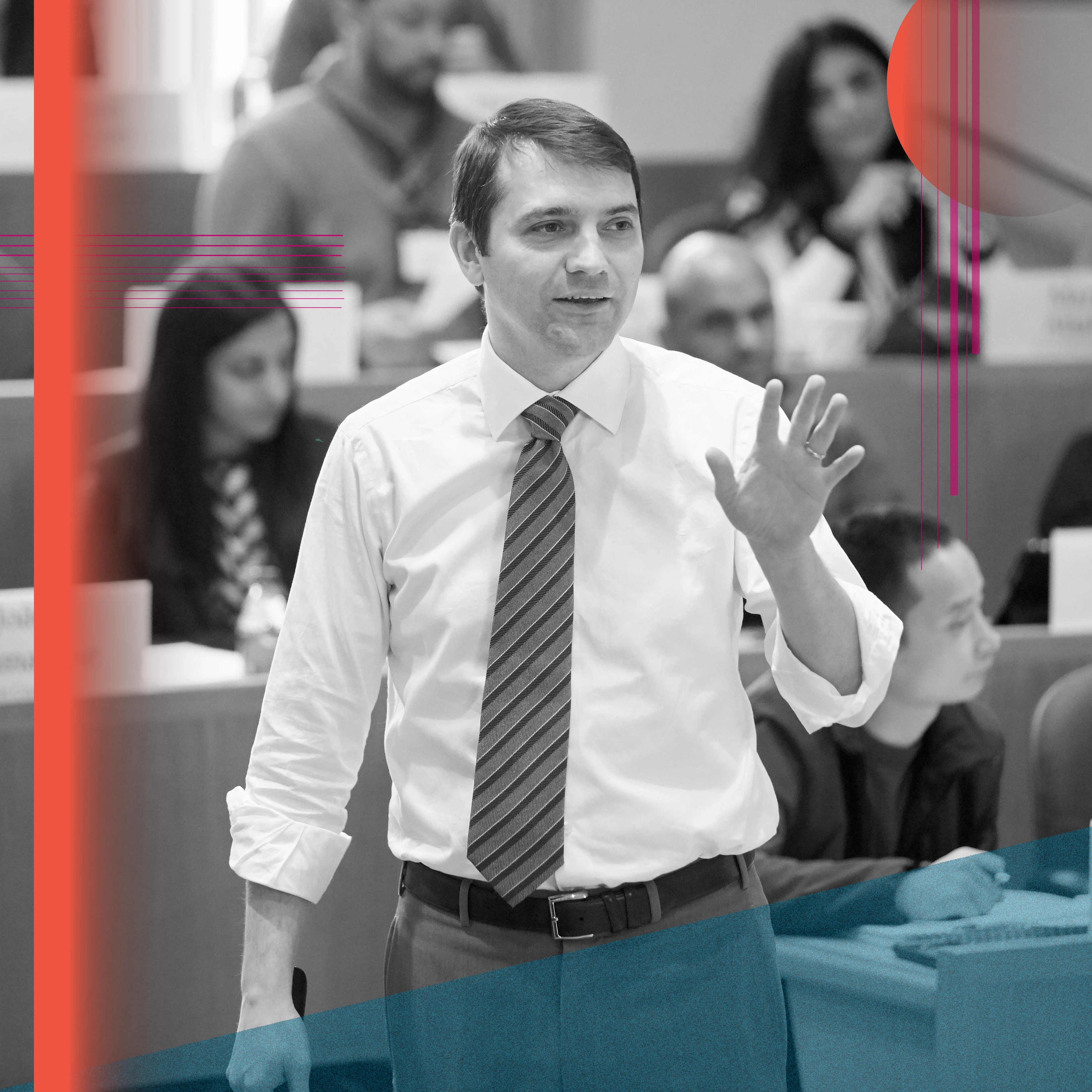 White male with white shirt and striped tie standing and holding up one hand as a gesture while speaking. Behind him students sit at desks in a lecture hall. Overlay of orange, teal and pink shapes.