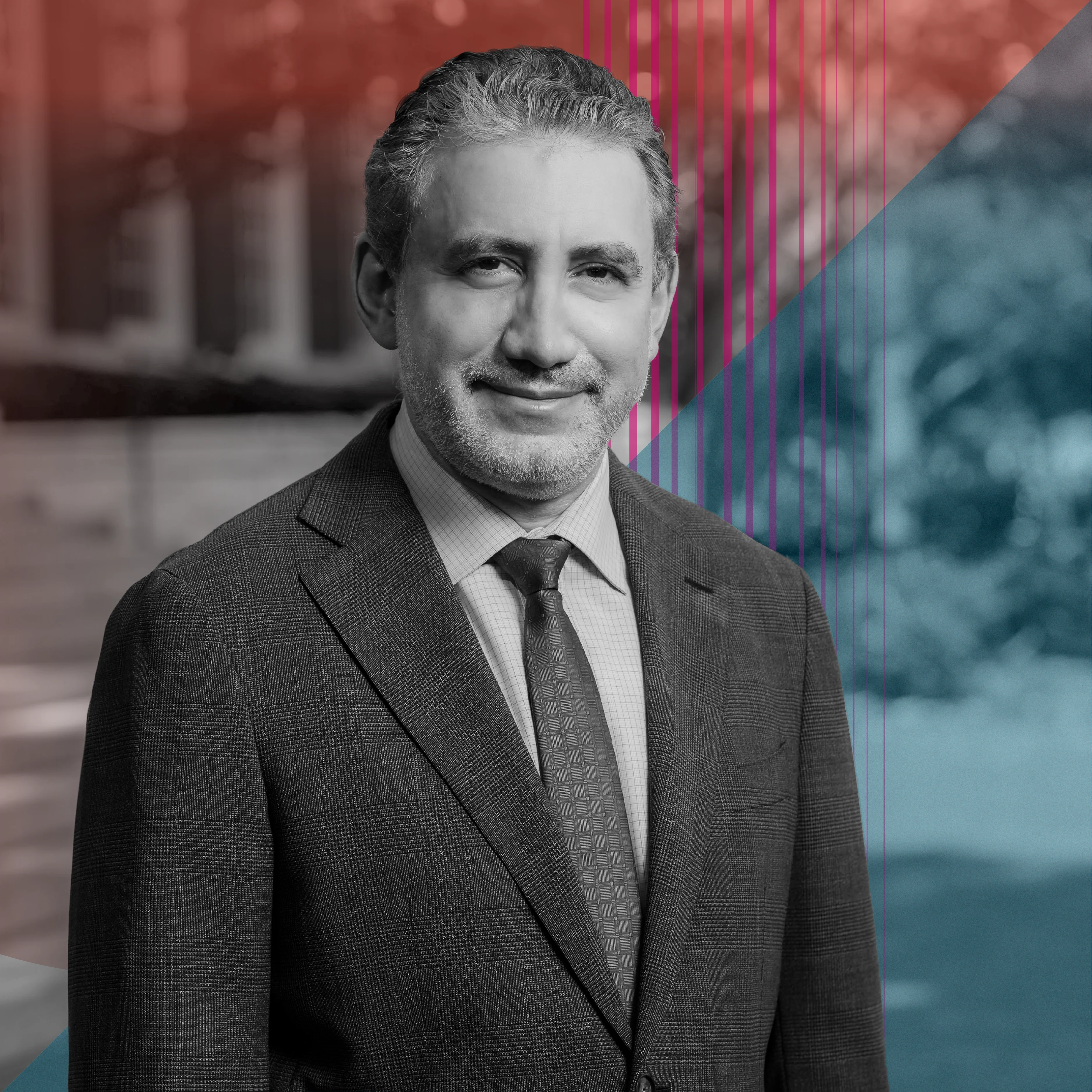 Black and white photo; middle-aged man with grey hair and close-cut beard outdoors, with a dark suit, checkered shirt and tie, facing the camera with a slight smile. Background of blurred buildings and trees, red and blue overlays, and thin vertical lines.