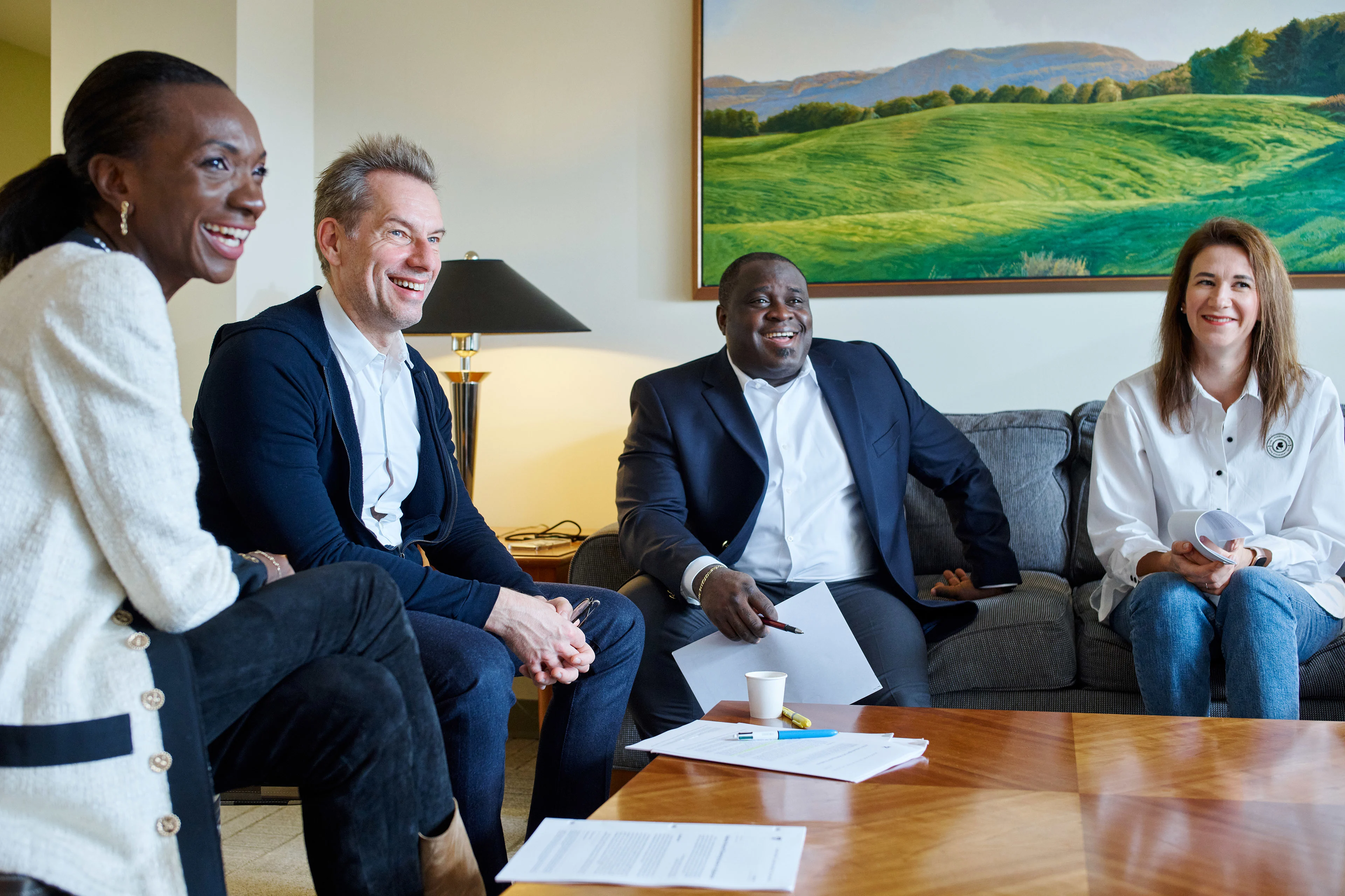 A diverse group of four executives laughing and engaging in a casual business meeting, seated around a wooden table with documents