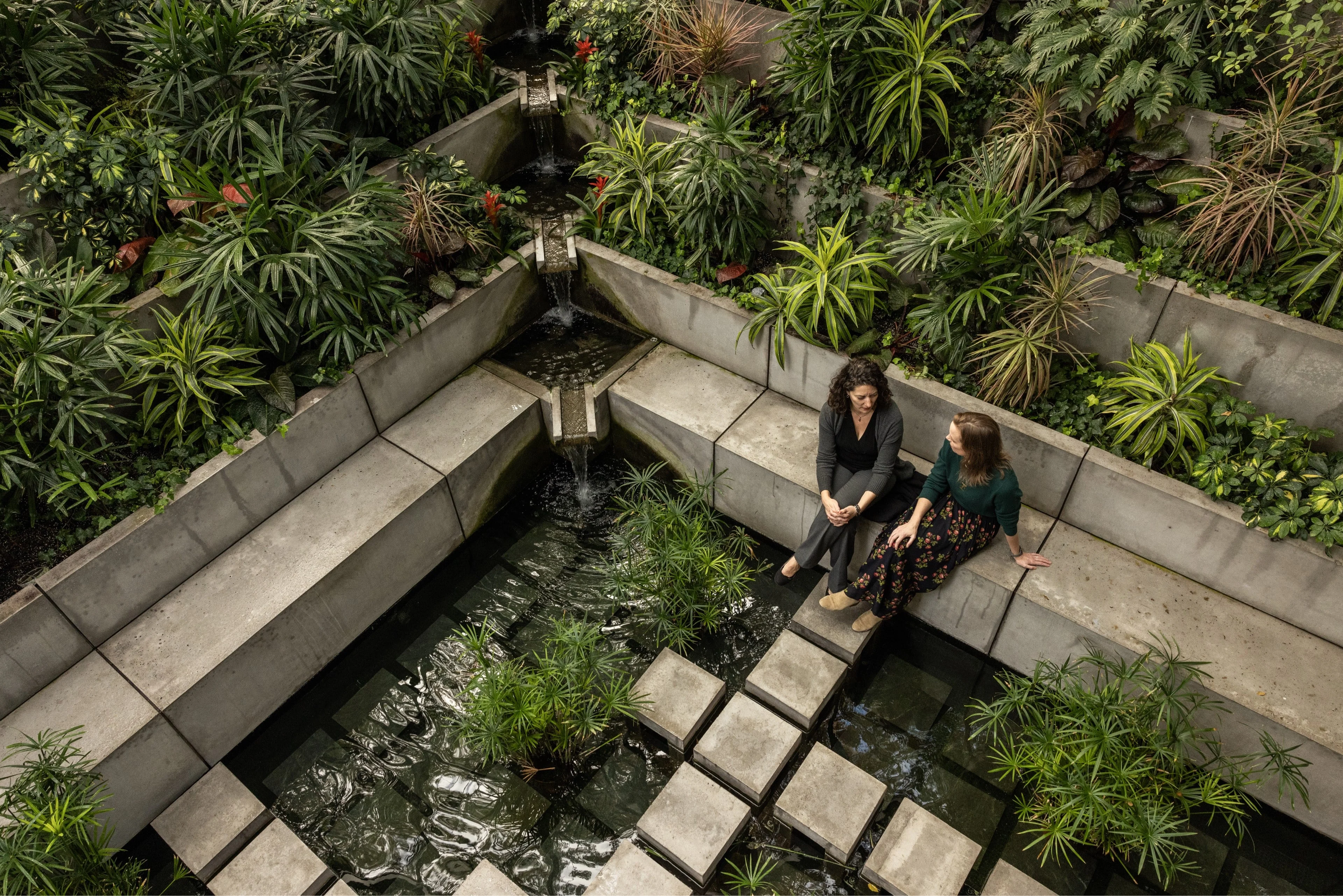 Two women talking by the water, surrounded by vegetation in the HBS Class of 1959 Chapel