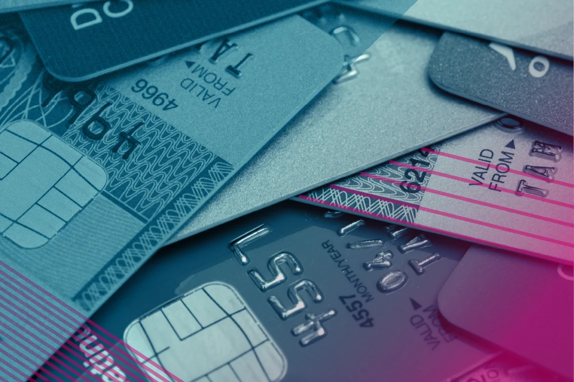 Close-up of overlapping credit and debit cards with visible chip and embossed numbers. The image is tinted blue with translucent geometric overlays and pink accent lines.