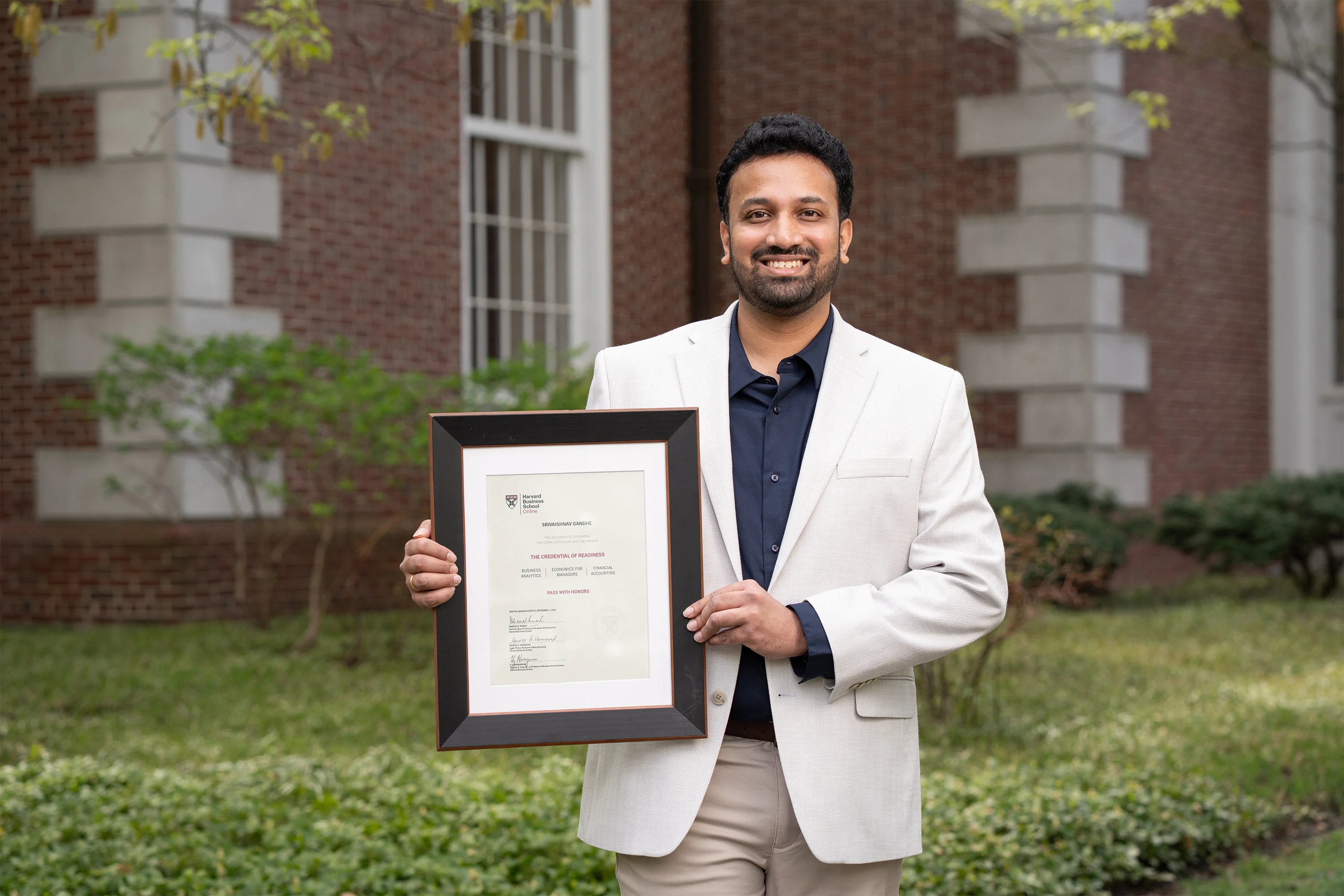 Person smiling and holding a framed certificate outside a brick academic building.
