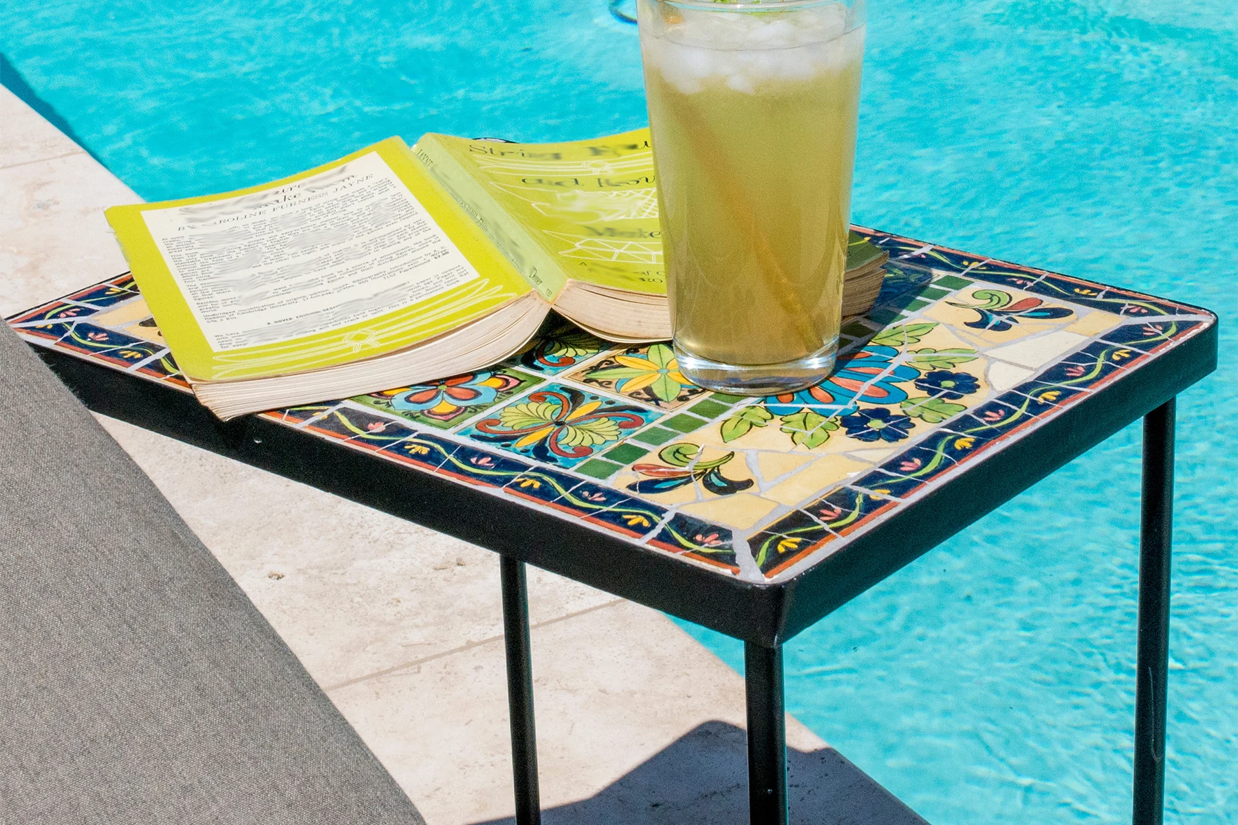 Poolside table with lemonade and an open, facedown yellow book upon it.