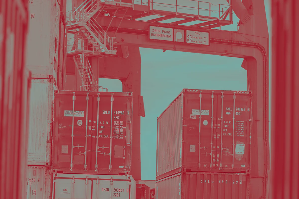 Duotone image with shipping containers waiting on a cement dock.