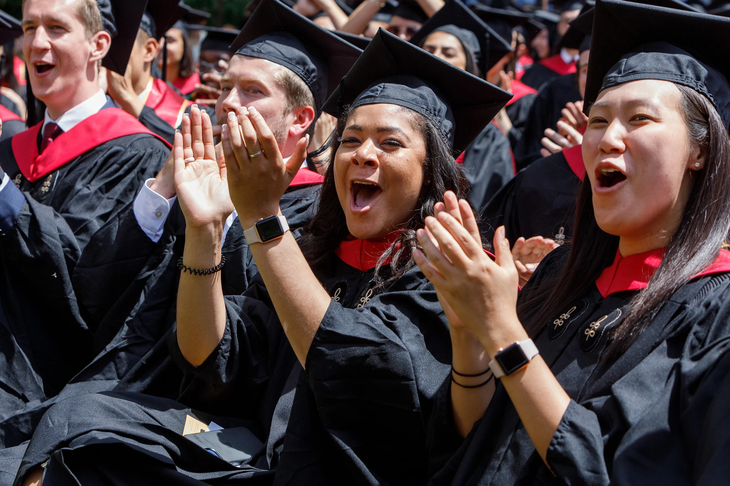 Graduates in cap and gown clapping seated in a crowd.