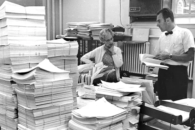 Harvard Business School staff members stacking printed case studies. 1939 milestone of 15,000 cases.