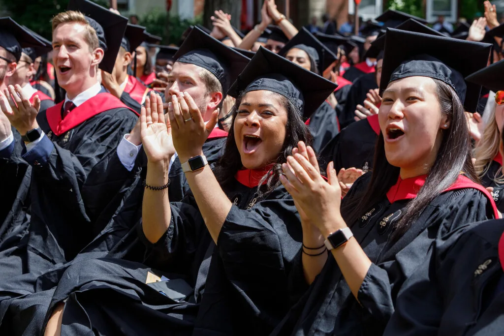 Graduates clapping and smiling in caps and gowns during a graduation ceremony.