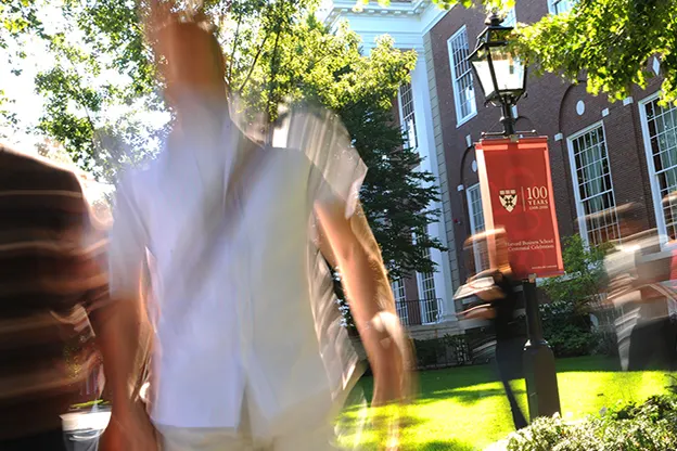 People walking outside Baker Library, 2008. A color banner celebrating Harvard Business School's 100th anniversary is seen on a lamppost.