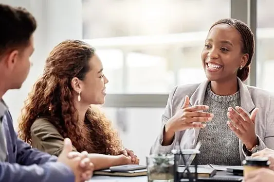 Four professionals sit at a table in discussion, with one person smiling and speaking while the others listen attentively.