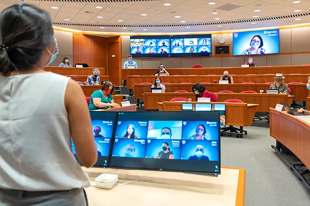 A hybrid classroom during COVID-19-a small number of masked students in the room, many monitors showing remote attendees, 2020.