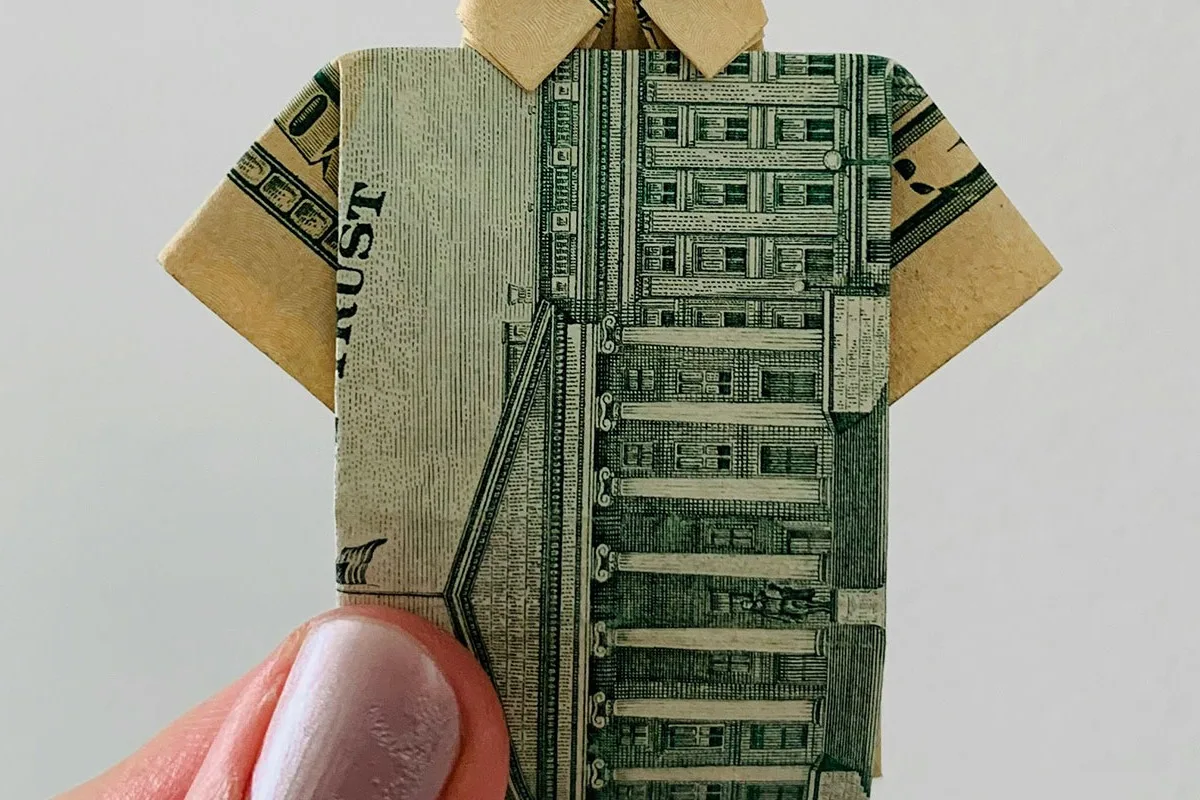 Hand holding a dollar bill folded into the shape of a shirt.