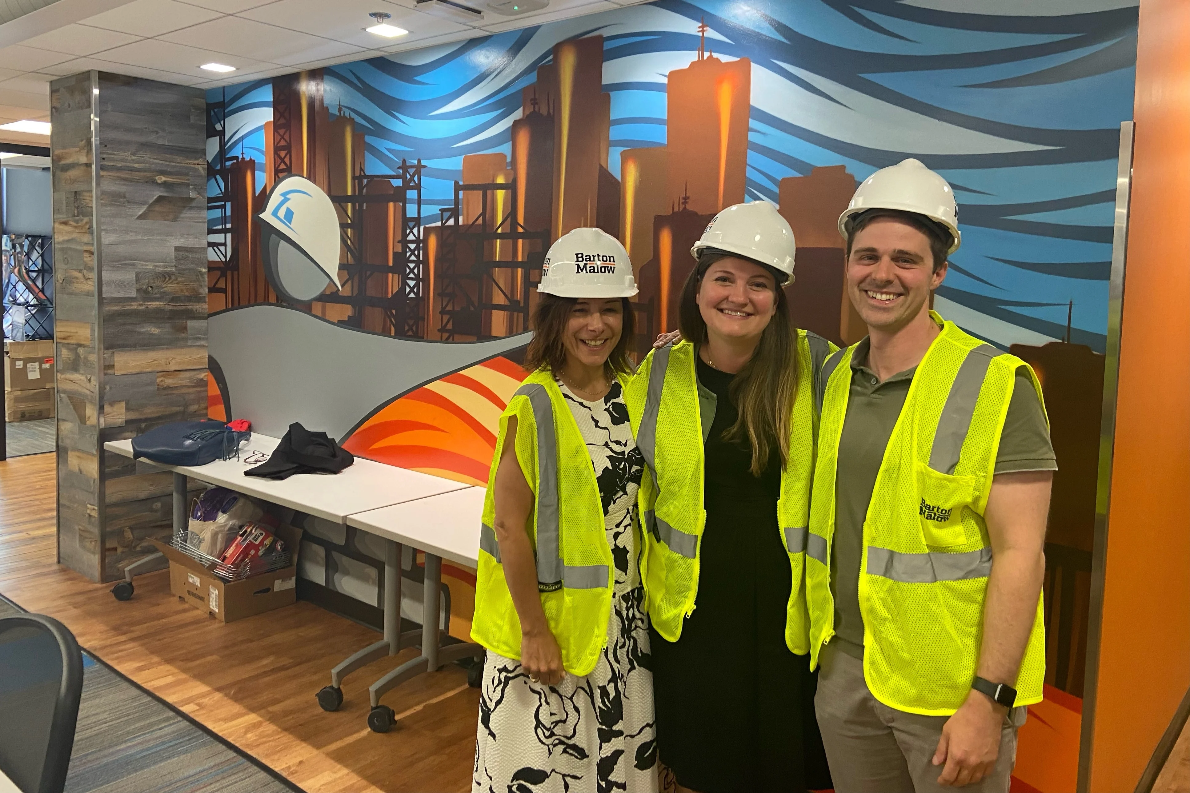 Three people wearing hard hats and yellow vests, standing together and smiling. 