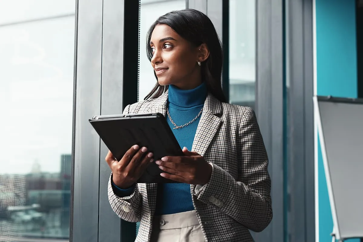 Business professional holding a tablet and looking out window in office.