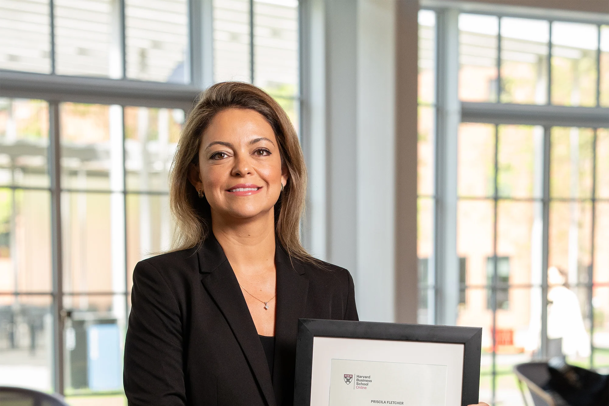 Individual smiling and holding a framed Harvard Business School Online certificate in a modern lounge area.