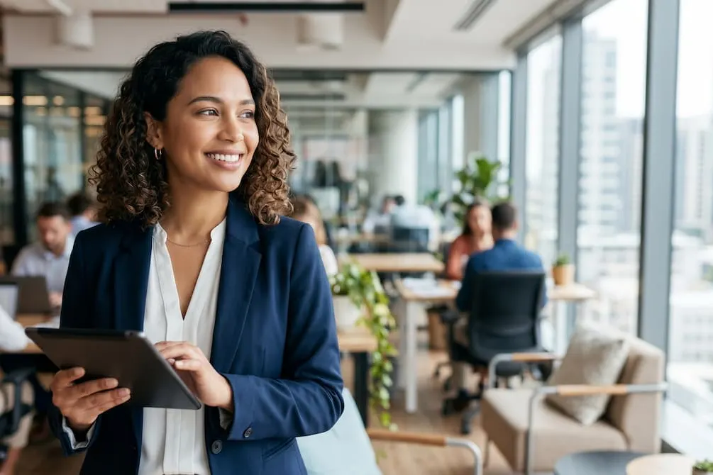 Business leader holding tablet in busy open plan office. 