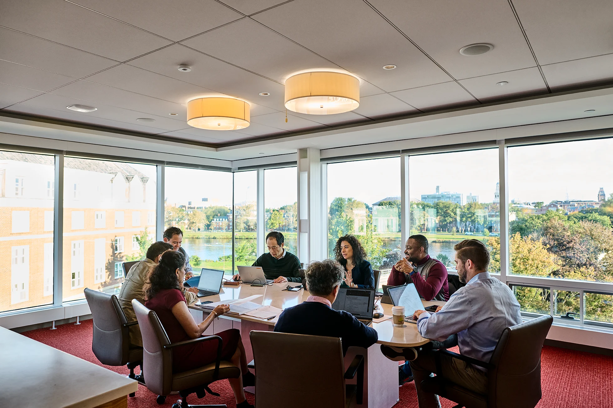 A group of executives working around a conference table in Tata Hall with HBS campus and Charles river view