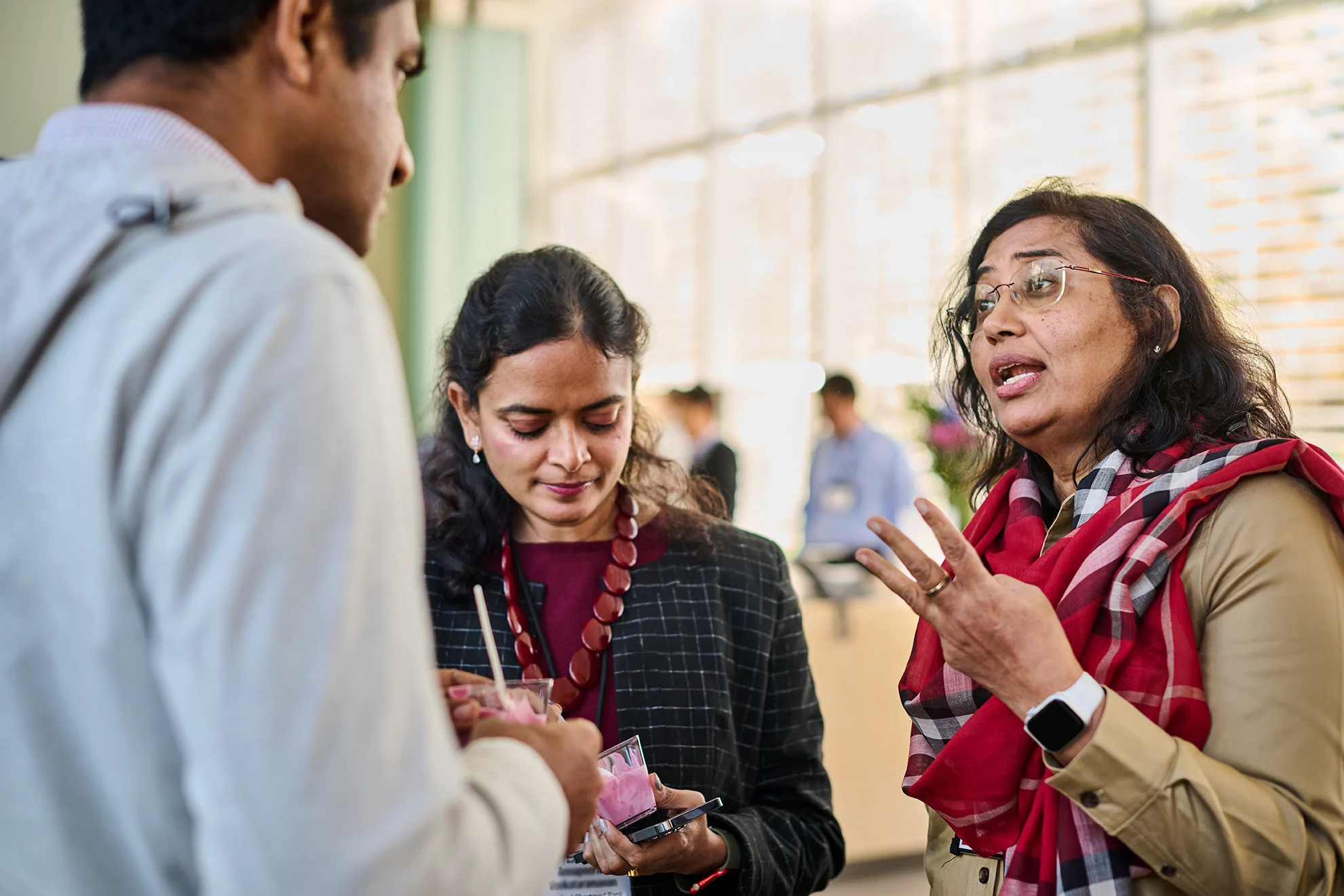 Three participants engaged in a discussion during the break. A woman in a red scarf gestures while speaking, as others listen attentively