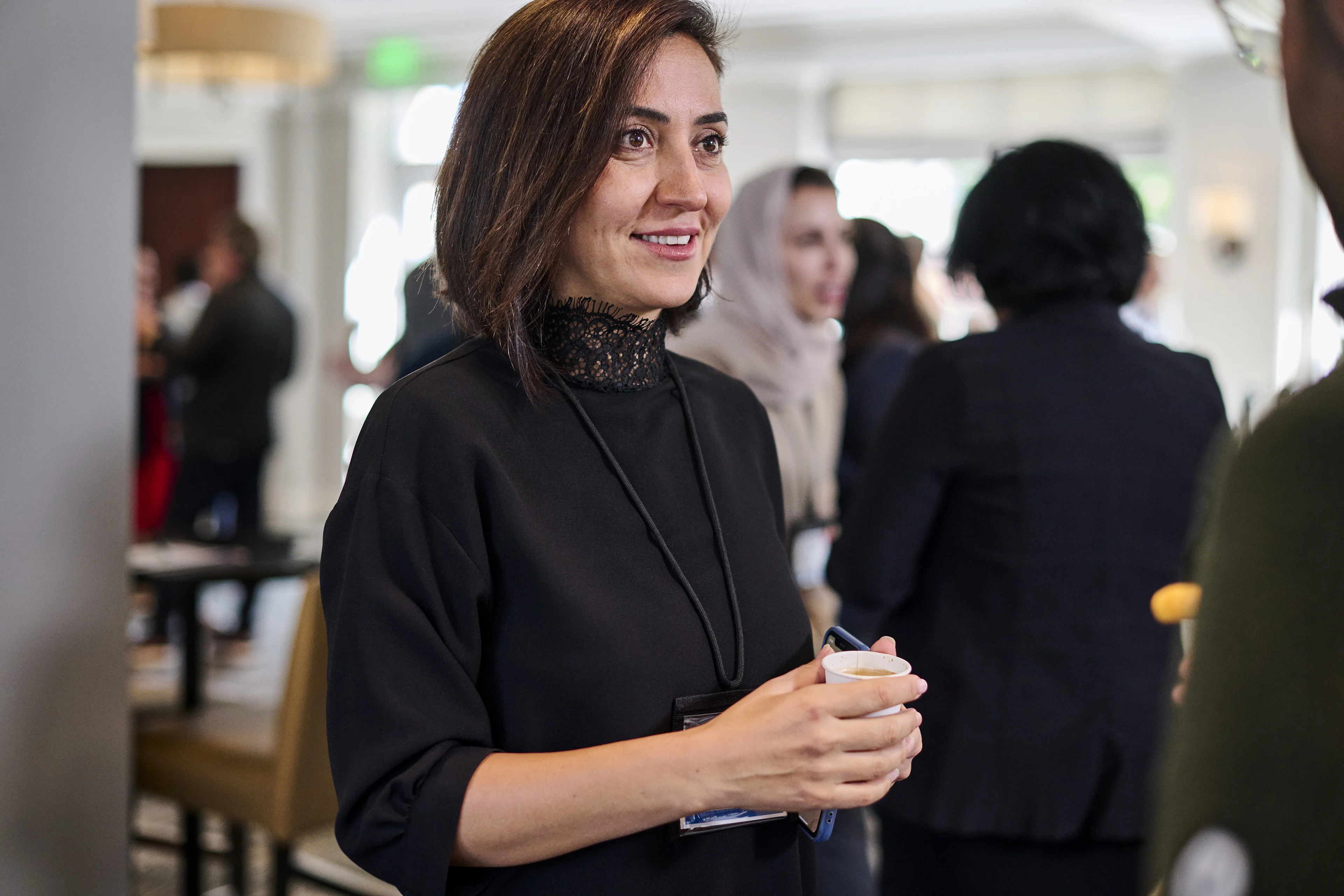 A woman wearing a black top engages in conversation with someone out of frame while several others socialize in the background
