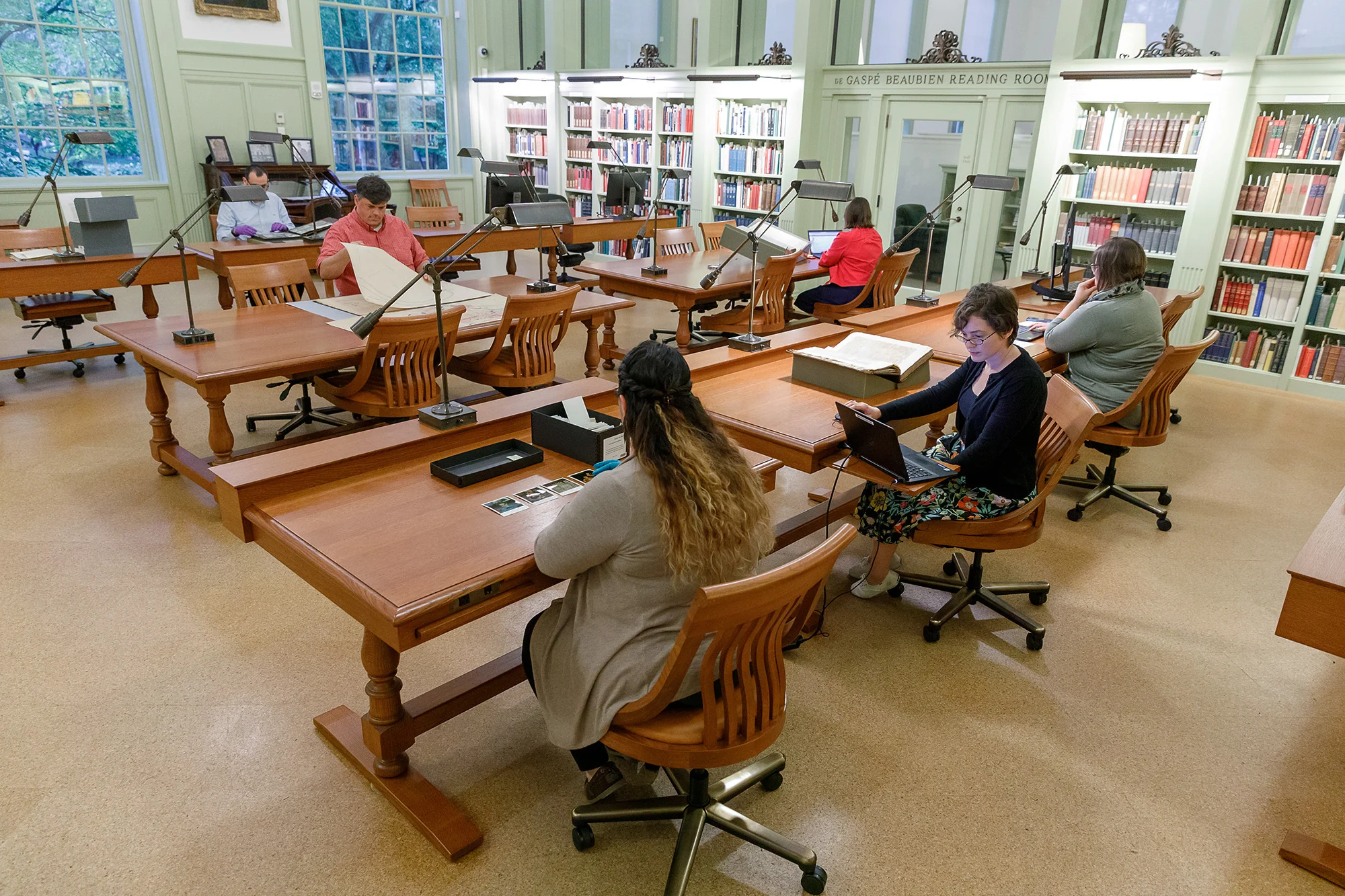 Room with wooden tables lined with bookshelves. People seated at many tables.