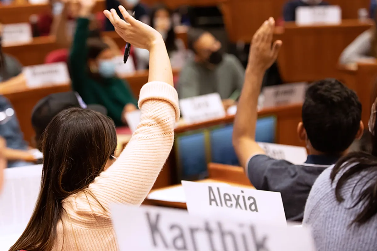 MBA students raise their hands to participate in a case discussion in a Harvard Business School classroom.