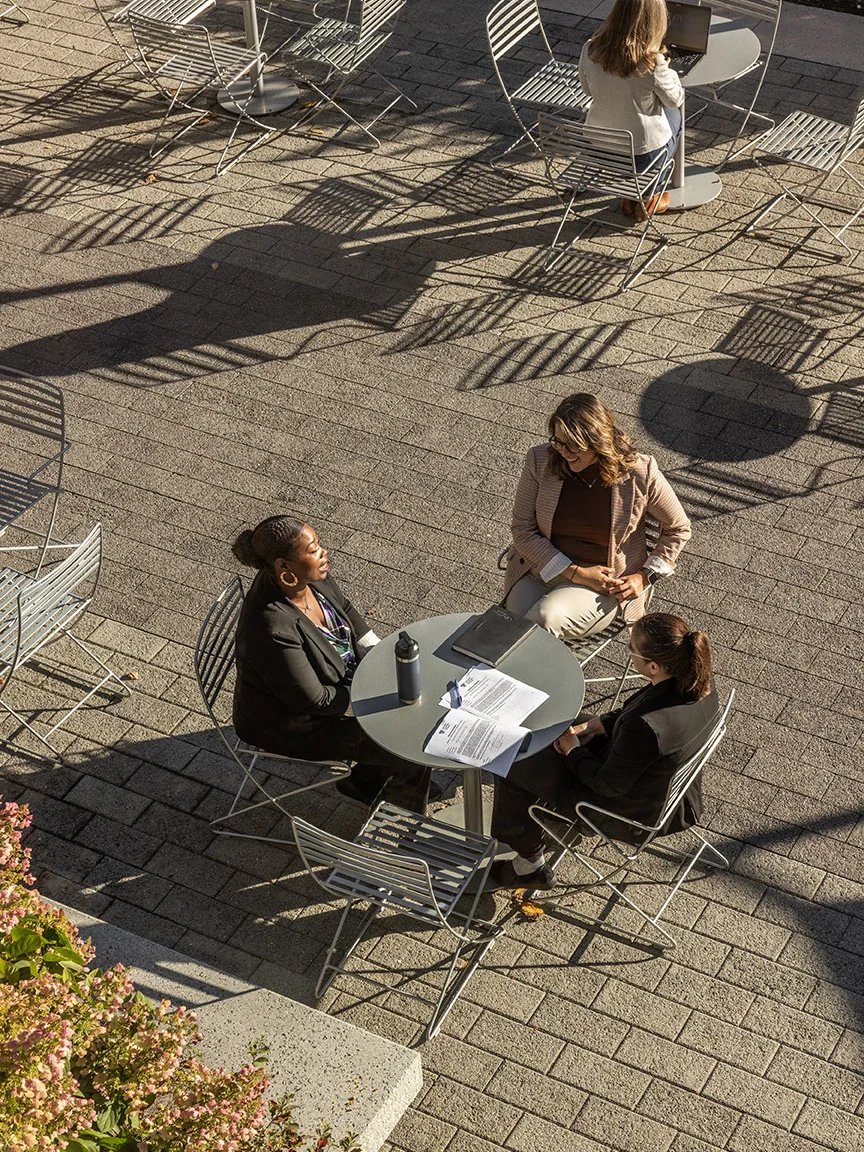 Aerial view of three executives sitting around a table outside on the HBS campus on a sunny day to review a case