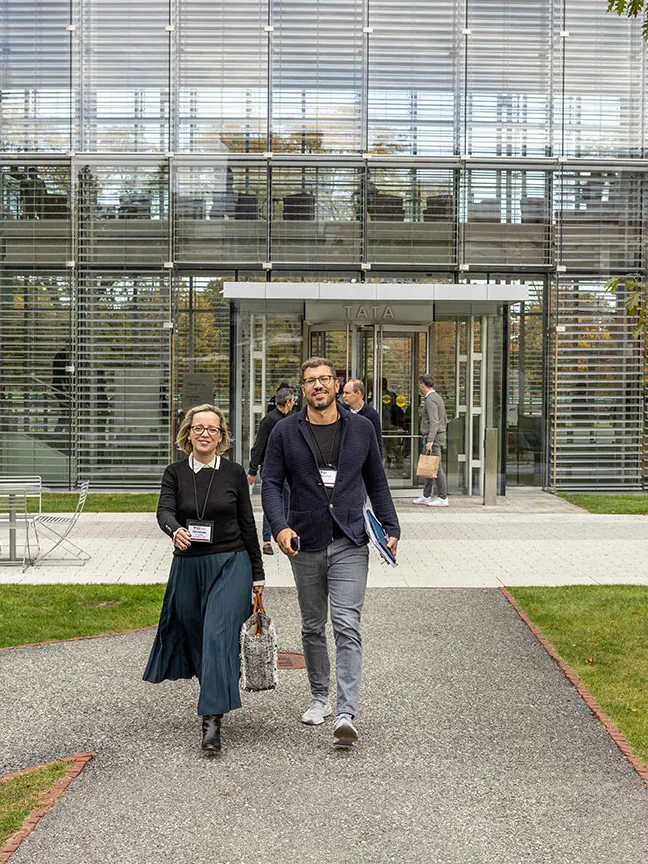 A male and a female executive walk outside the Tata building and onto the main Harvard Business School campus