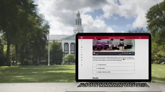 A laptop open to the HBS Online website sits outside with the view of an academic building in the background
