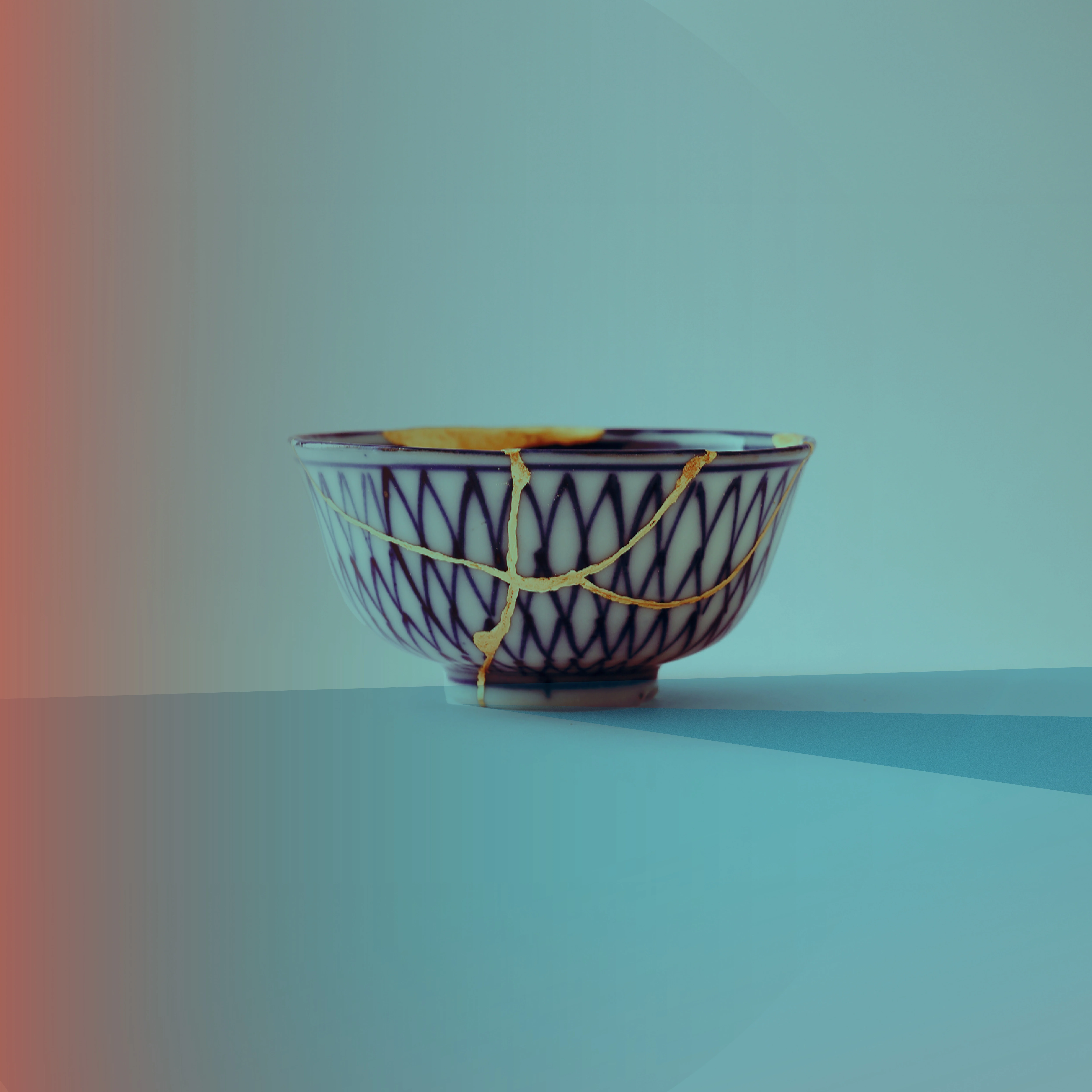 Cracked blue and white ceramic bowl with kintsugi-style repairs against a teal background with faded red along the left side.