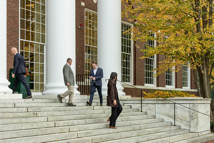 Three male executives and one female executive walk on the steps of Baker Library