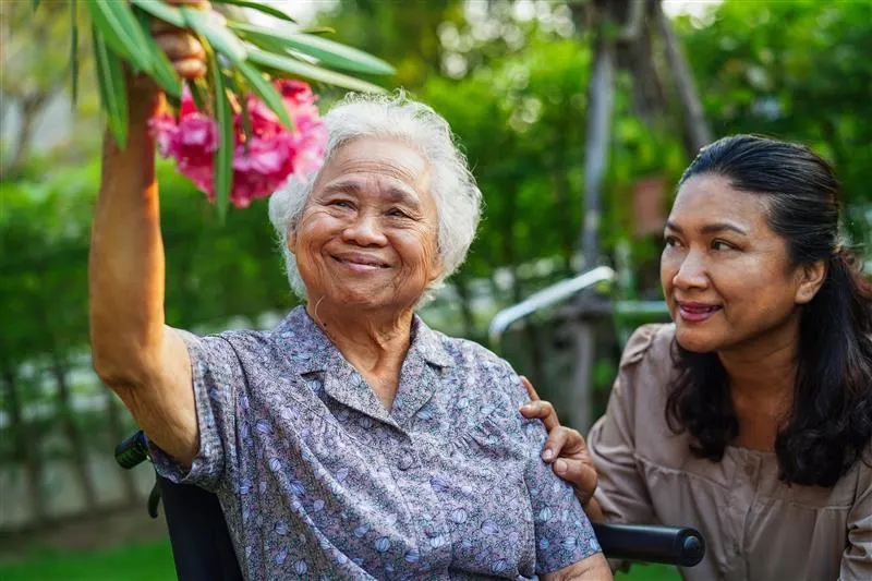 Elderly woman in wheelchair looking at flower with daughter