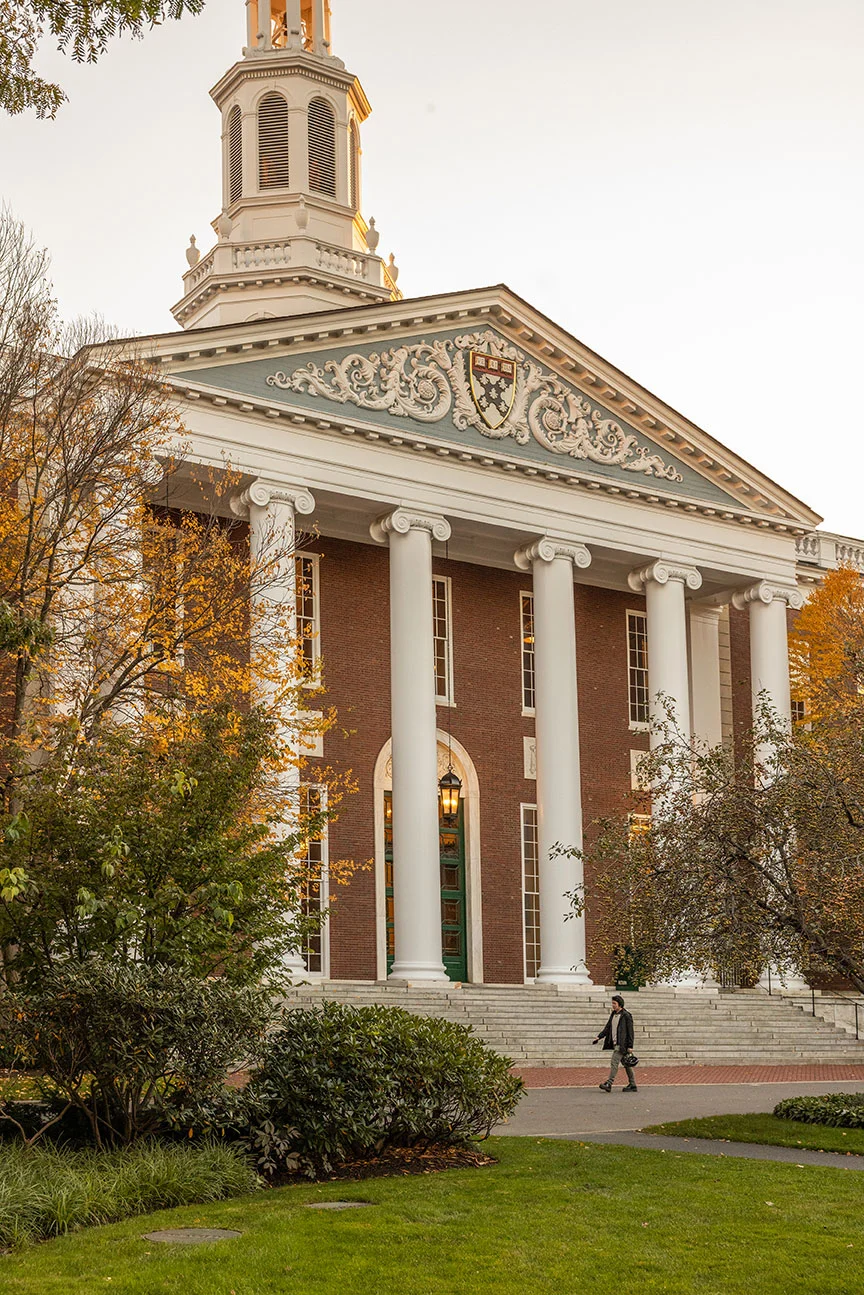 A male executives walks in front of the main steps to Baker Library 