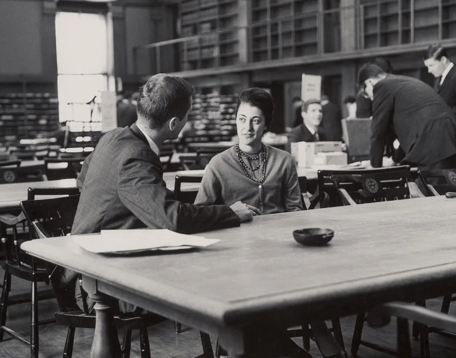 Michelle Roos inquires about club activities from a second year student in Baker Library reading room, circa 1964