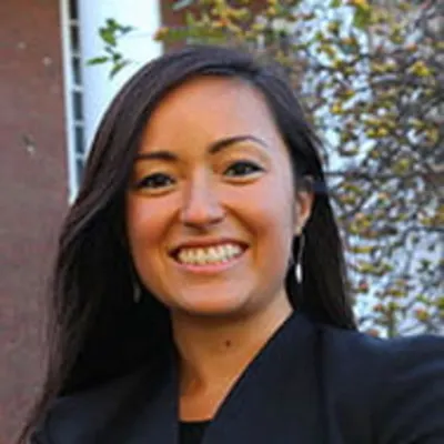 A woman with dark hair in dark clothing smiling. 
