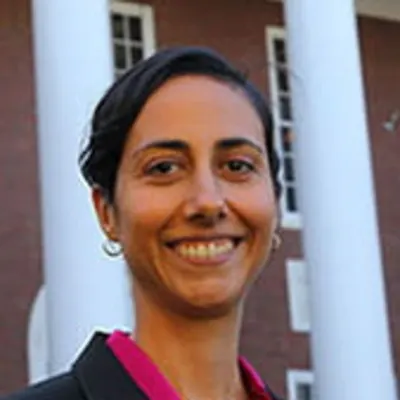 A woman with her hair pulled back in a black blazer with a magenta shirt, smiling.