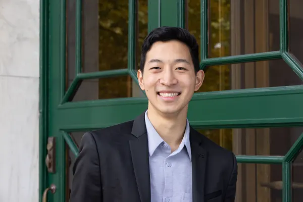 A young man in a suit and tie smiles confidently at the camera.