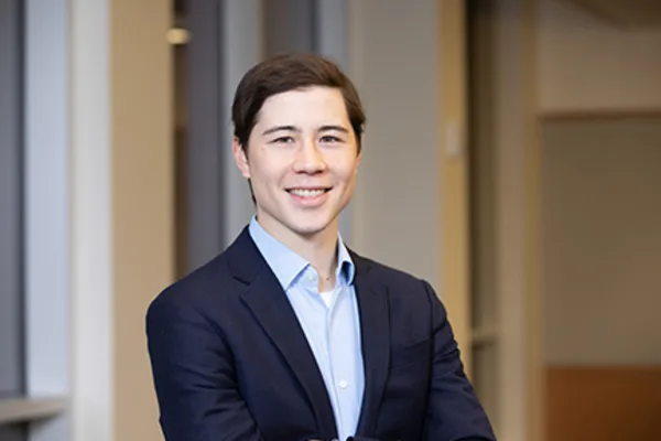 A young man in a suit and tie smiles confidently at the camera.