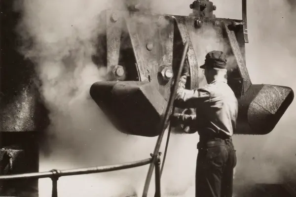 Steelworker operates heavy machinery amid rising steam inside an industrial foundry.