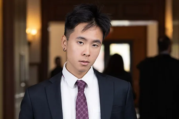 A young man in a suit and tie stands confidently in a well-lit hallway.