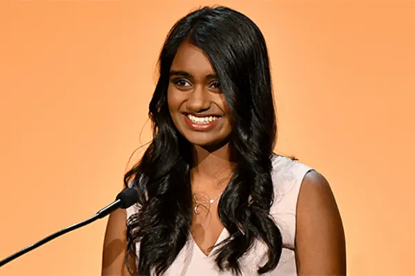 A woman smiles confidently while standing at a podium, engaging with her audience during a presentation.