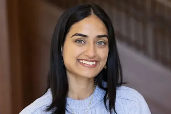 Person with straight black hair wearing a light blue sweater, smiling in front of a staircase background.