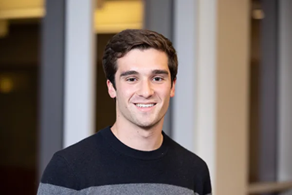 A young man wearing a sweater smiles warmly at the camera, exuding a friendly and approachable demeanor.