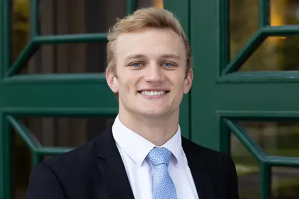 Person in a suit and light blue tie smiling in front of a green-framed glass door.