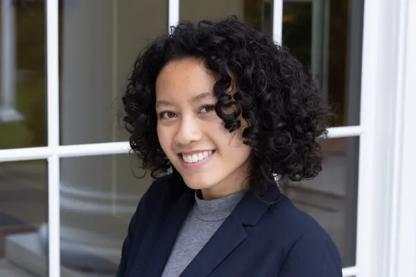 A woman with curly hair in a suit smiles confidently at the camera.